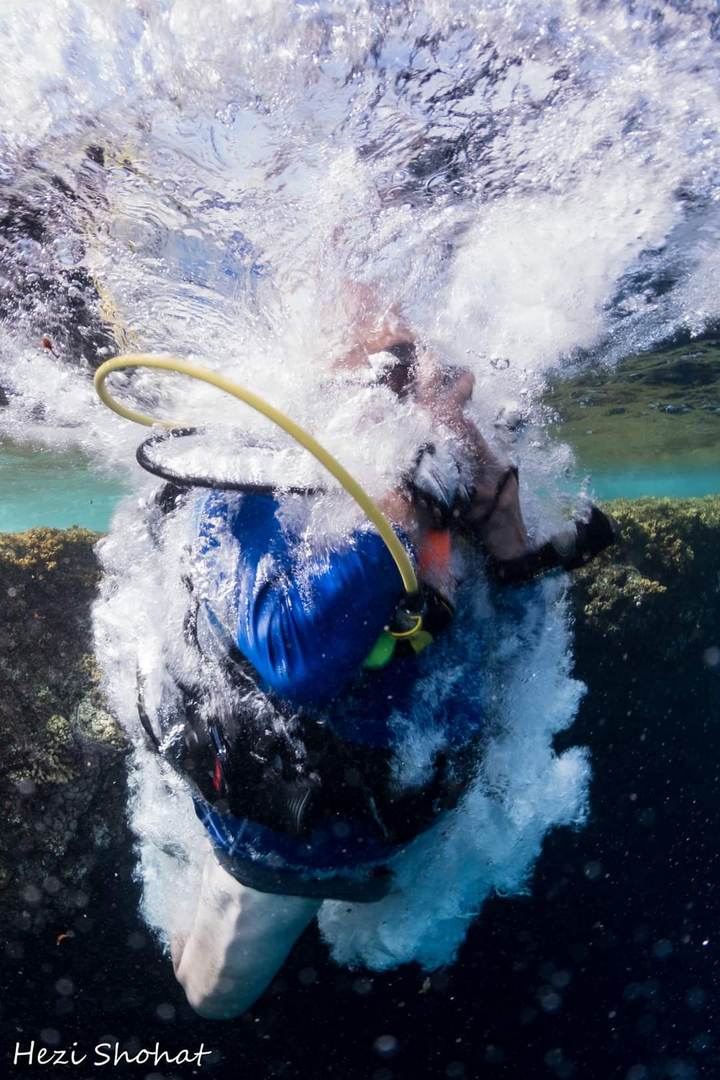 Ein Taucher springt ins Wasser, umgeben von weißen Luftblasen, von unten fotografiert