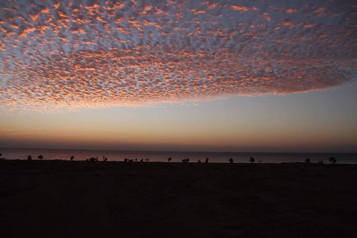Rosa und orange getupfte Wolken in der Abenddämmerung über dem Meer