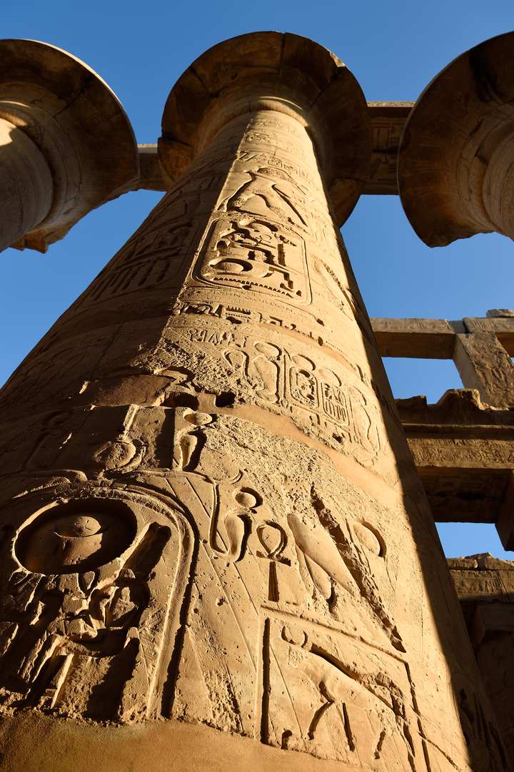 Mächtige, mit Hieroglyphen verzierte Säulen im Karnak-Tempel vor blauem Himmel
